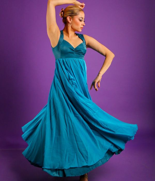 Woman performing a fluid, graceful cardio movement in a dark studio with teal light.